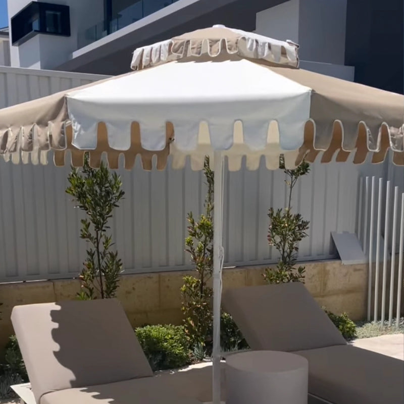 A customer's umbrella over garden loungers beside a timber screen