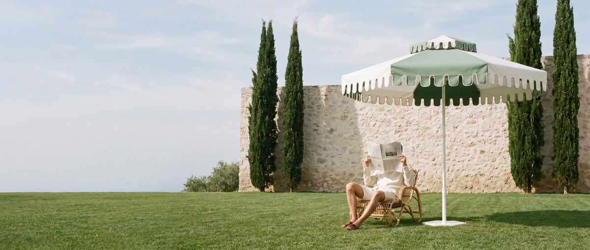 A man reading the paper under a Cactus Green umbrella by a stone villa wall