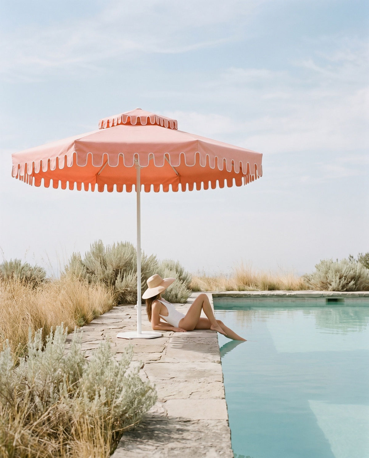 A woman resting beside a pool under a Flamingo Blush umbrella