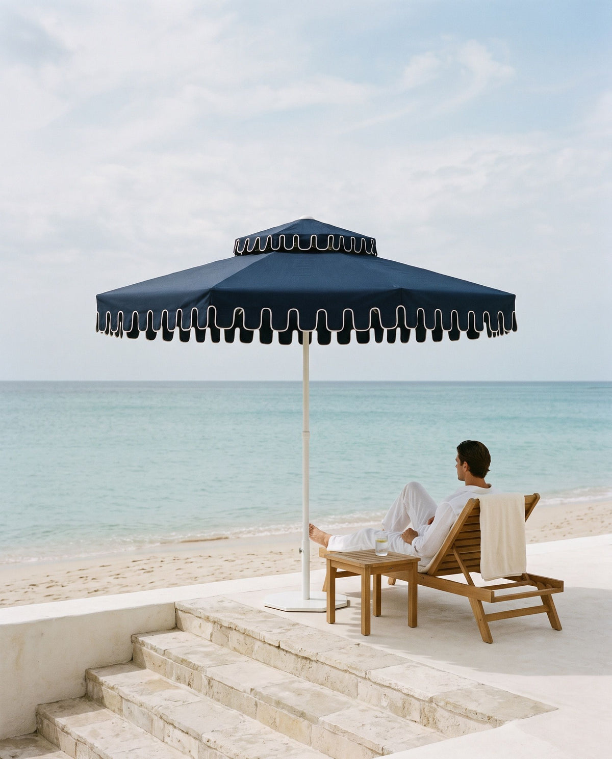 A man in a deck chair under a Midnight Navy umbrella on a beach-club terrace
