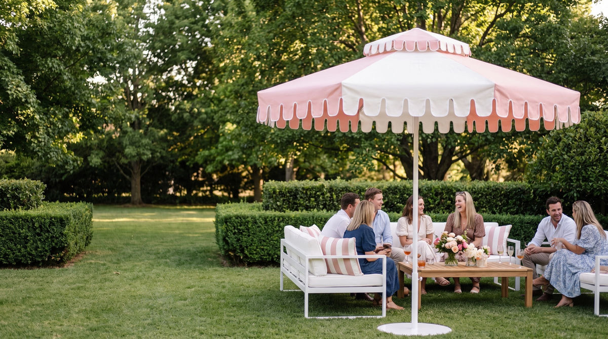 A Powdered Blush umbrella over a white lounge setting with guests beside clipped hedges