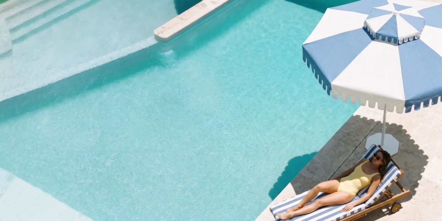 A Provence Blue umbrella over a lounger beside a pool, seen from above